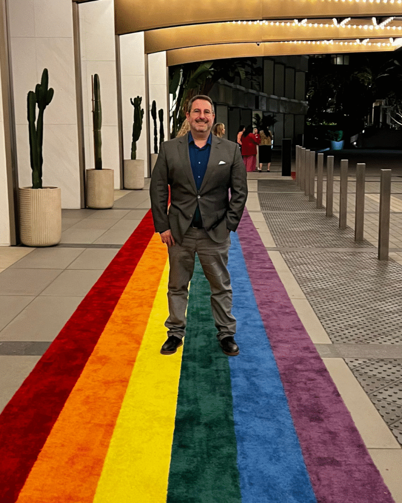An image of Josh Scheer, President and owner of White Lotus Travel Design, standing on a rainbow carpet.