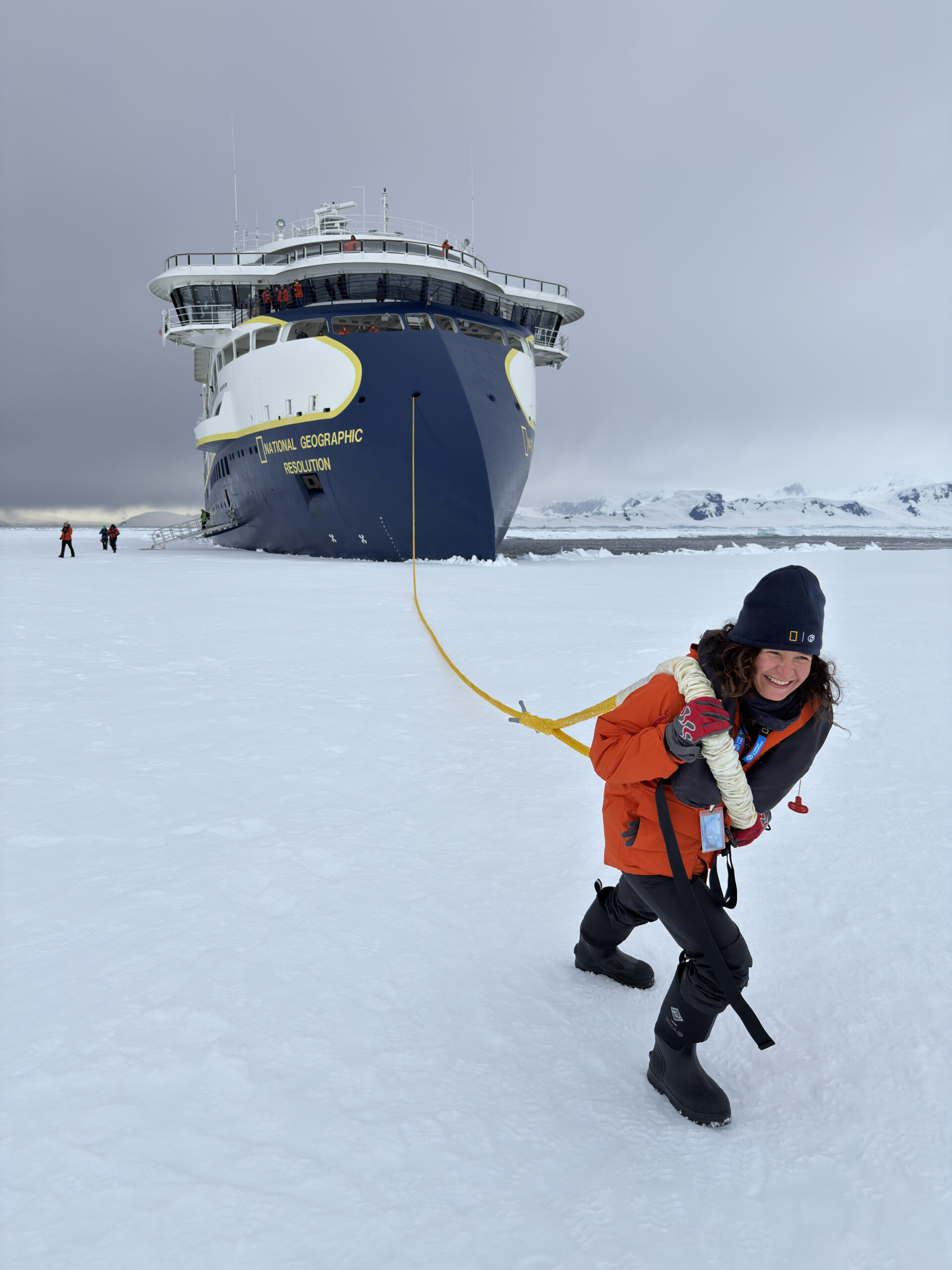 A woman in Antarctica laughing while pretending to tow the National Geographic Resolution, an expedition cruise ship.