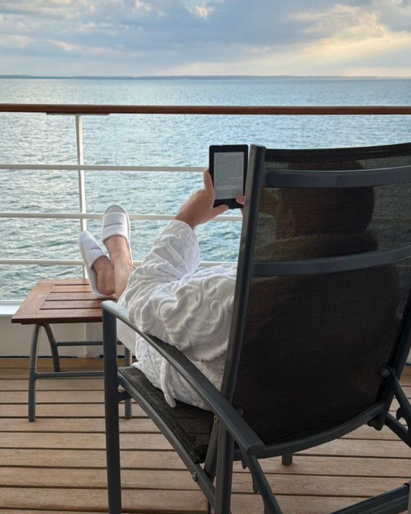 A man in his Silversea robe and slippers reading on his cruise suite's veranda